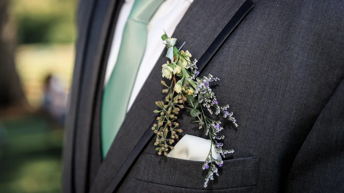 A man's suit jacket with a white pocket square and a floral arrangement pinned to the left side of his chest.